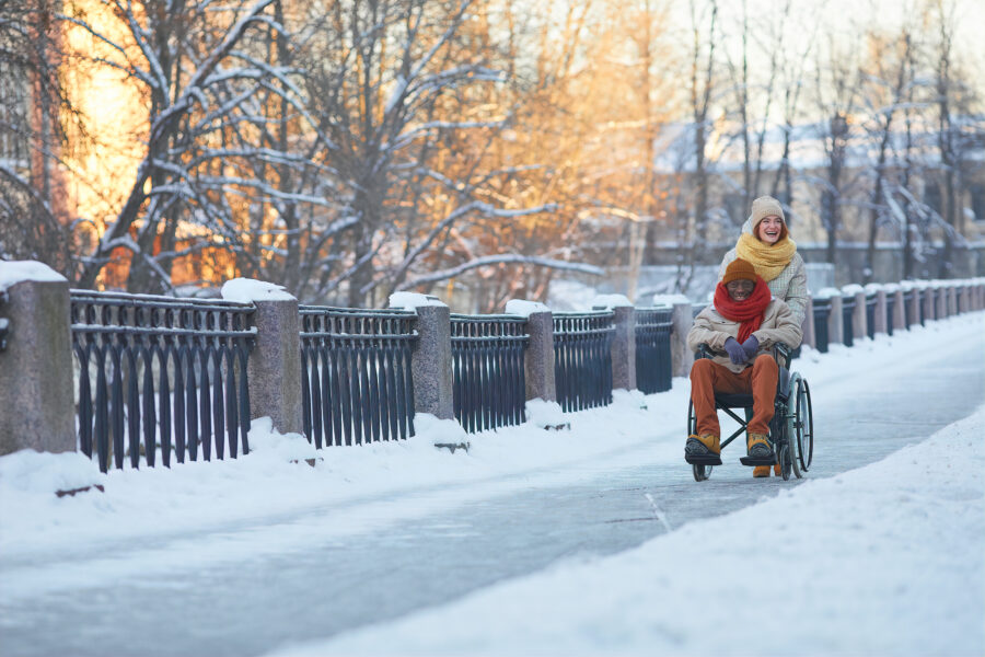 Young man in a wheelchair on a shoveled sidewalk in winter with his friend
