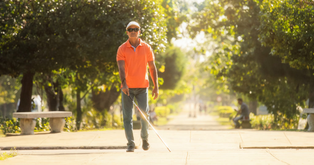 Hispanic blind man, latino people with disability, handicapped person and everyday life. Visually impaired man with walking stick, crossing the street.